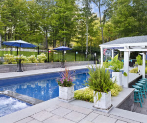 View of the pool, poolside bar, and pool house. Dex by Terra landscape and hardscape project in Westminster, MA.