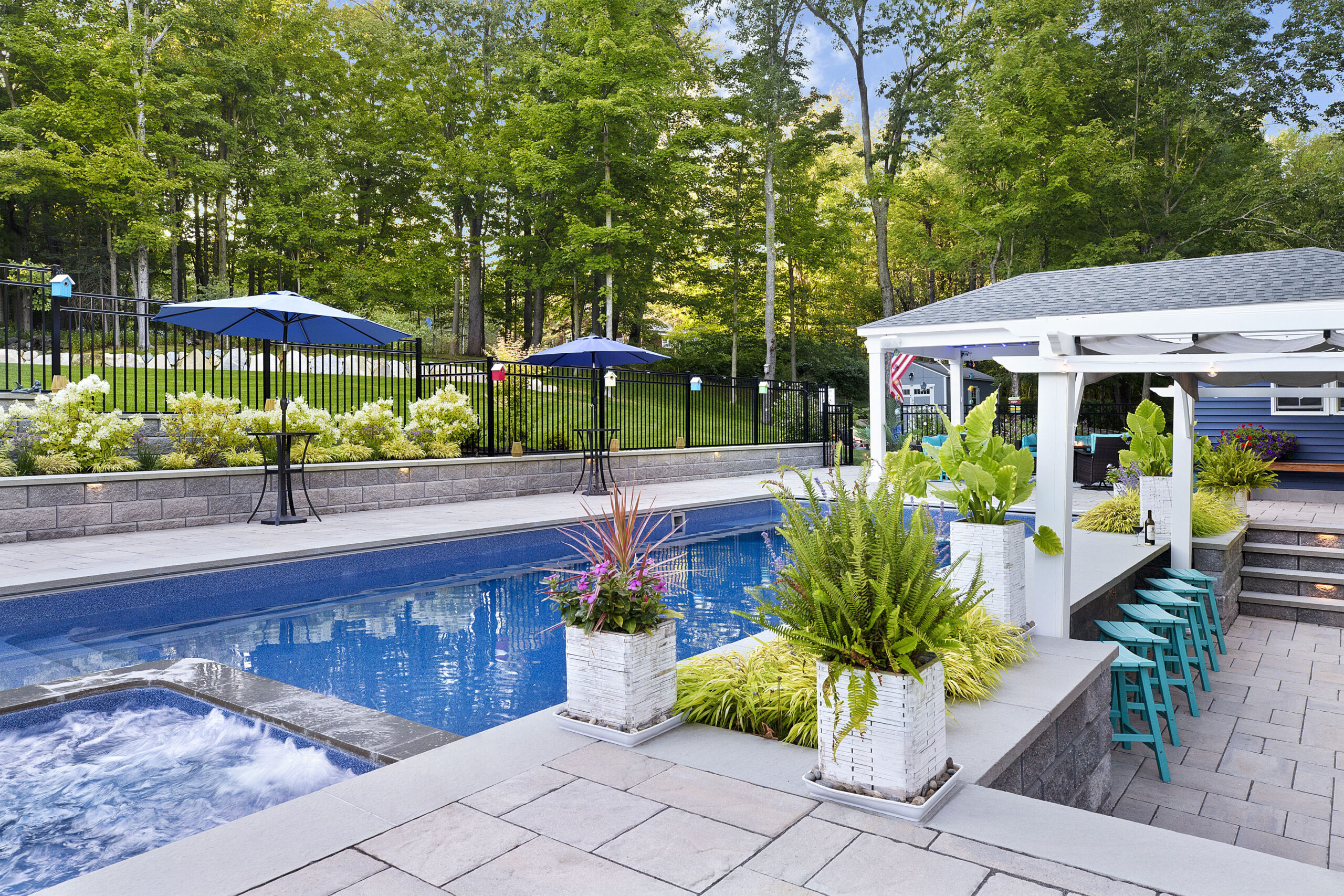 View of the pool, poolside bar, and pool house. Dex by Terra landscape and hardscape project in Westminster, MA.