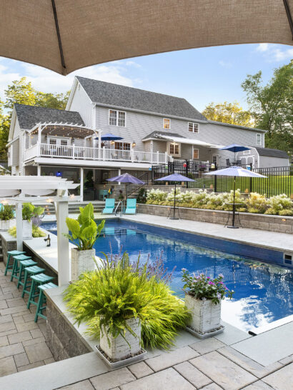 View of the pool, poolside bar, and back of the home. Dex by Terra landscape and hardscape project in Westminster, MA.