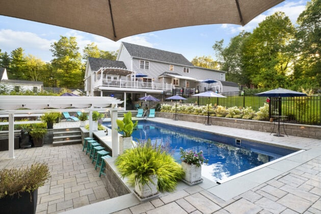 View of the pool, poolside bar, and back of the home. Dex by Terra landscape and hardscape project in Westminster, MA.