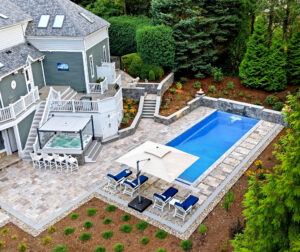 Drone view of pool deck, patio, hot tub bar, and landscaping surrounding the pool. Dex by Terra Hardscaping and Landscaping project in Lincoln, MA.