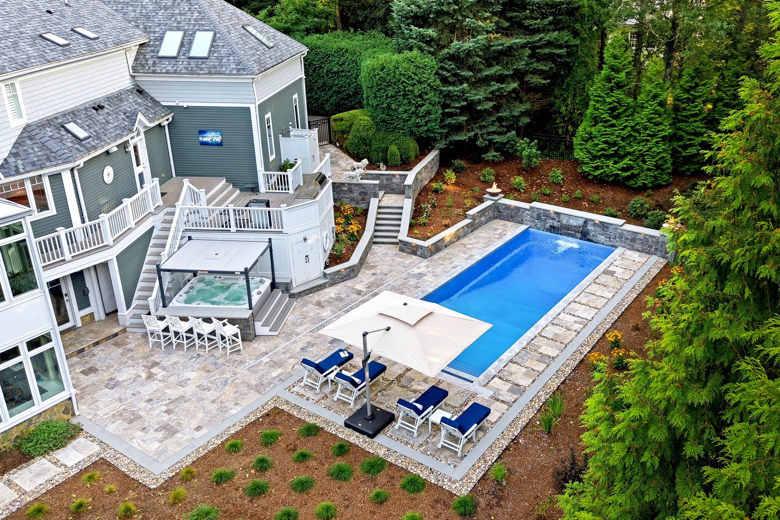 Drone view of pool deck, patio, hot tub bar, and landscaping surrounding the pool. Dex by Terra Hardscaping and Landscaping project in Lincoln, MA.