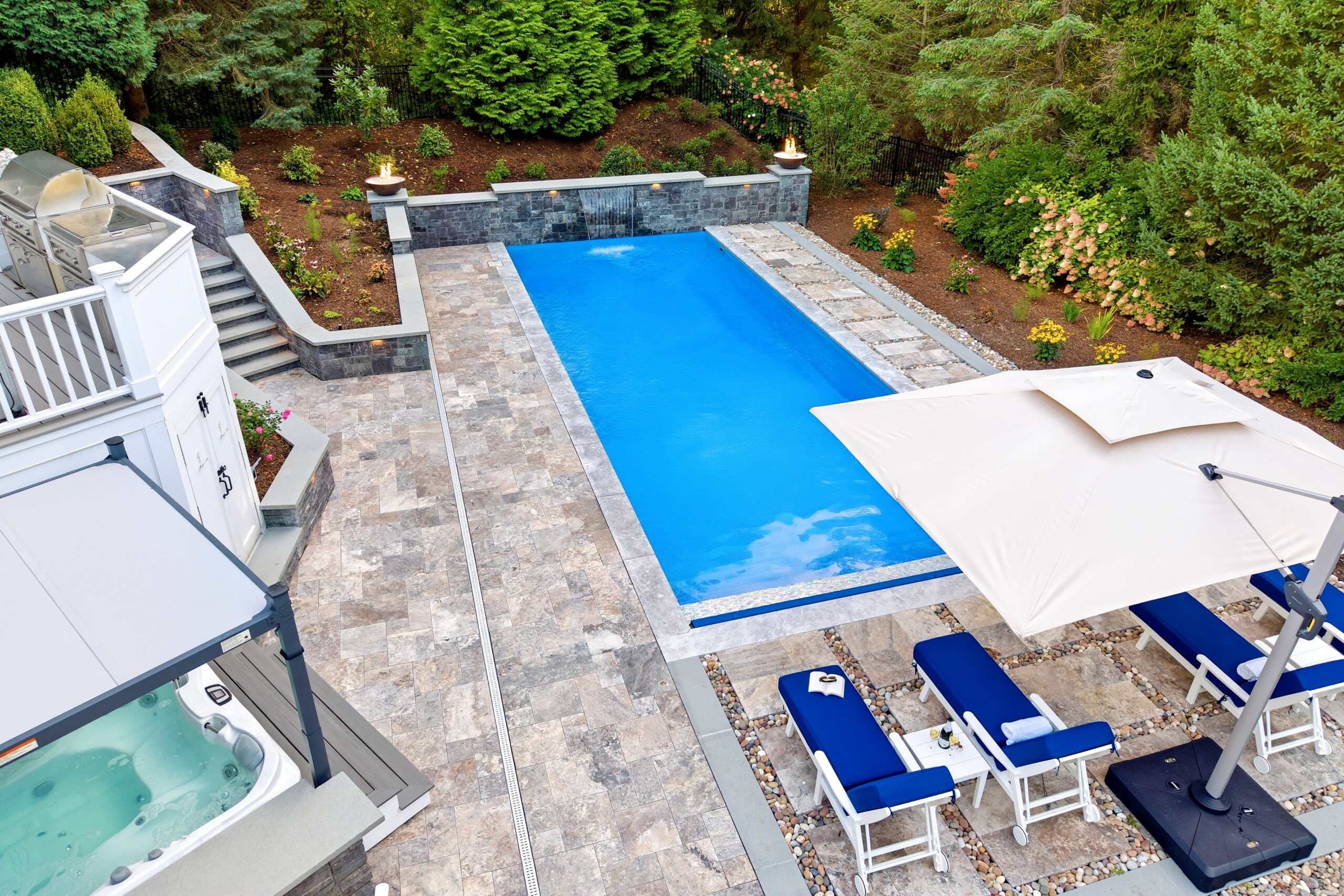 Drone view of pool deck, patio, hot tub bar, and landscaping surrounding the pool. Dex by Terra Hardscaping and Landscaping project in Lincoln, MA.