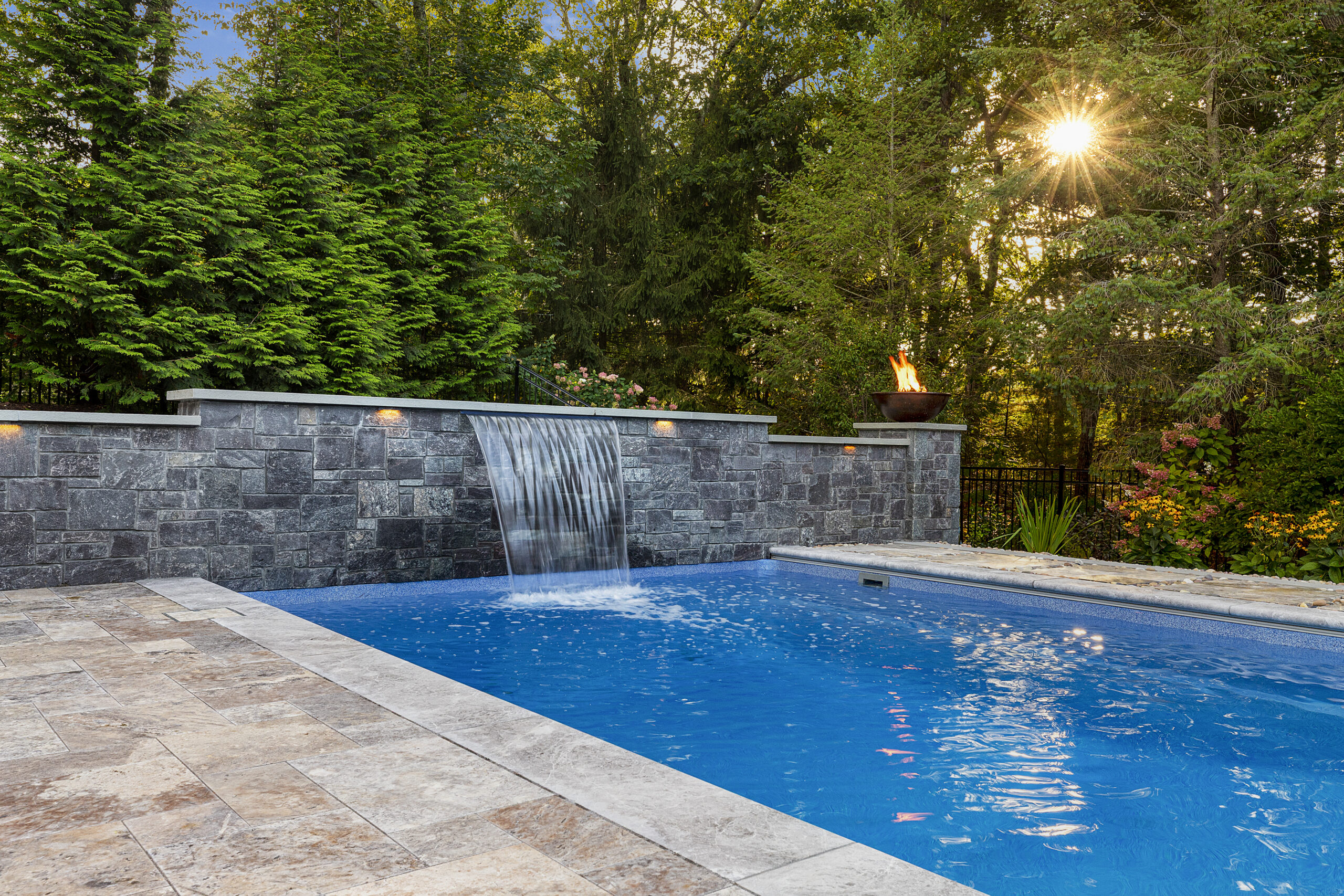 Water and fire features adorn the stone veneer wall on one end of the pool. Dex by Terra hardscape project in Lincoln, MA.
