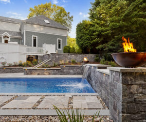Water and fire features adorn the stone veneer wall on one end of the pool. Dex by Terra hardscape project in Lincoln, MA.