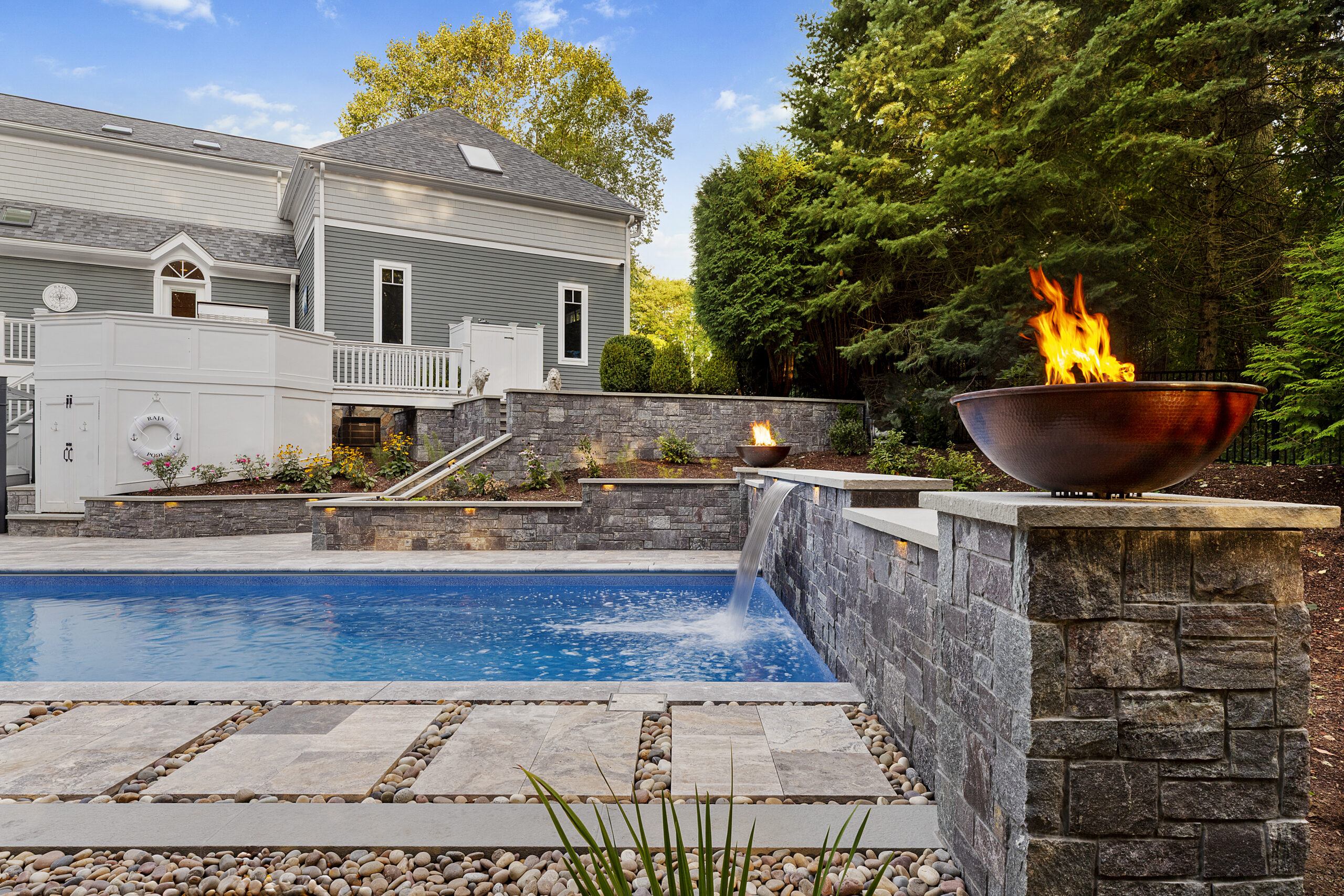 Water and fire features adorn the stone veneer wall on one end of the pool. Dex by Terra hardscape project in Lincoln, MA.