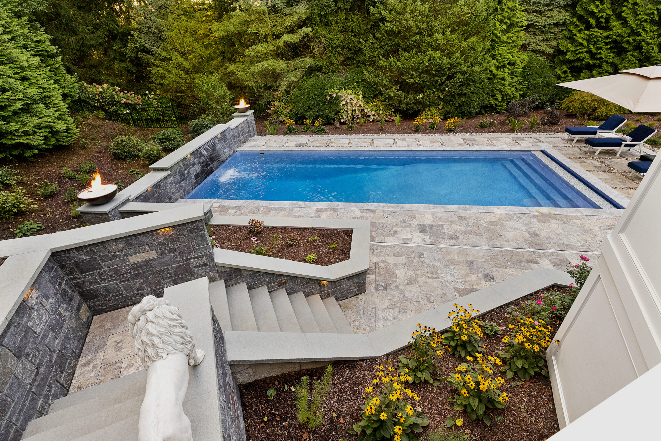 View of the pool from the top of the stone stairs with landscaping. Dex by Terra hardscape project in Lincoln, MA.