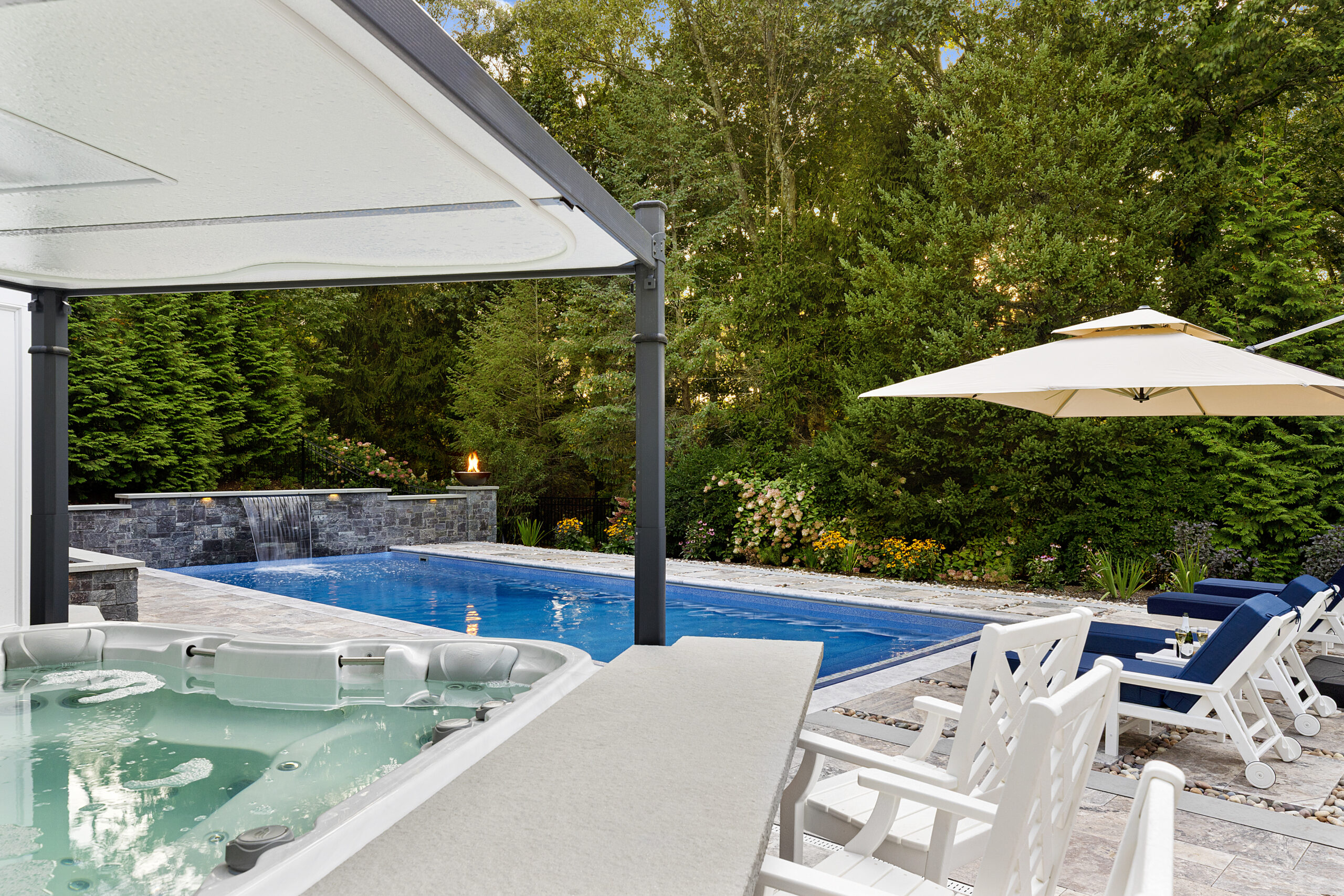 The hot tub bar area with the pool area and pool chairs in the background. Dex by Terra hardscape project in Lincoln, MA.