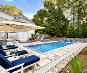 The pool area with pool chairs and an umbrella for shade. Dex by Terra hardscape project in Lincoln, MA.