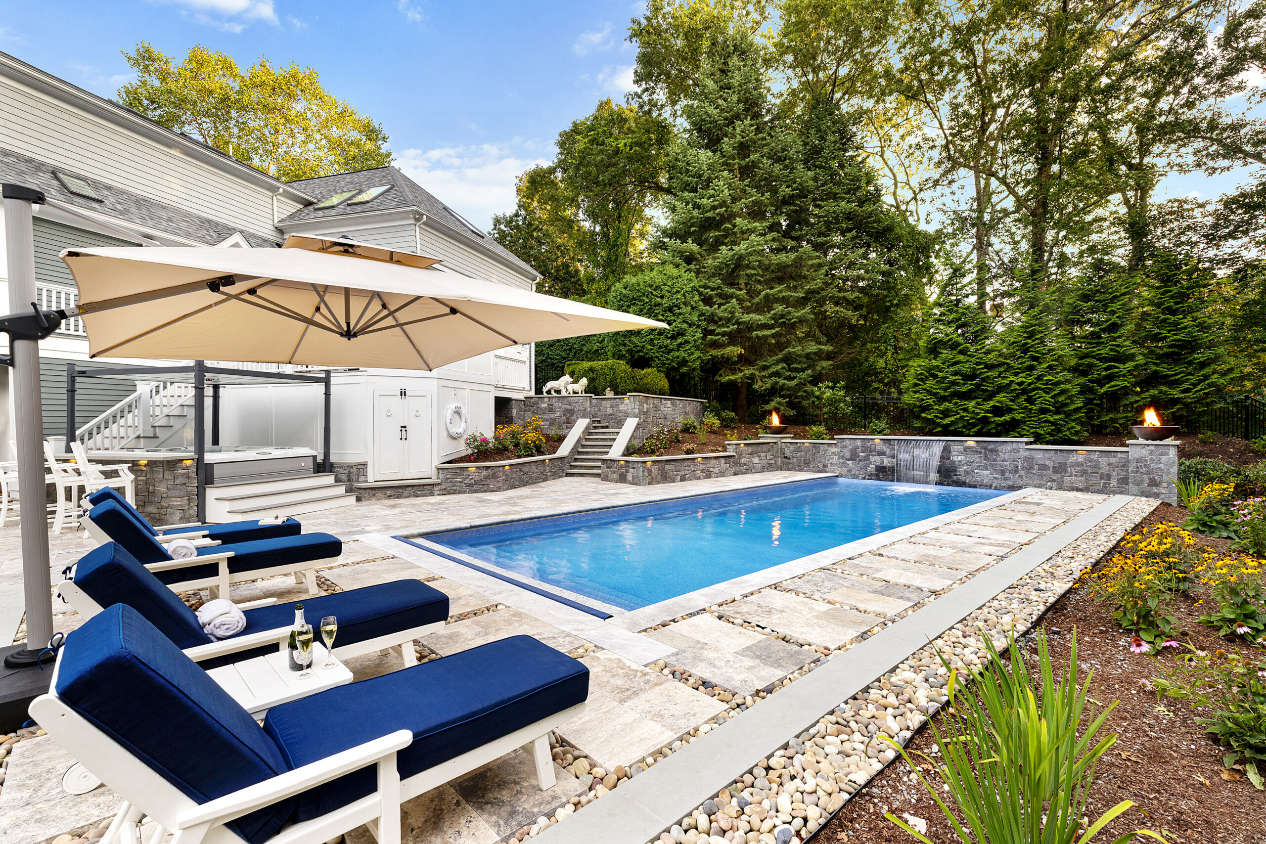 The pool area with pool chairs and an umbrella for shade. Dex by Terra hardscape project in Lincoln, MA.