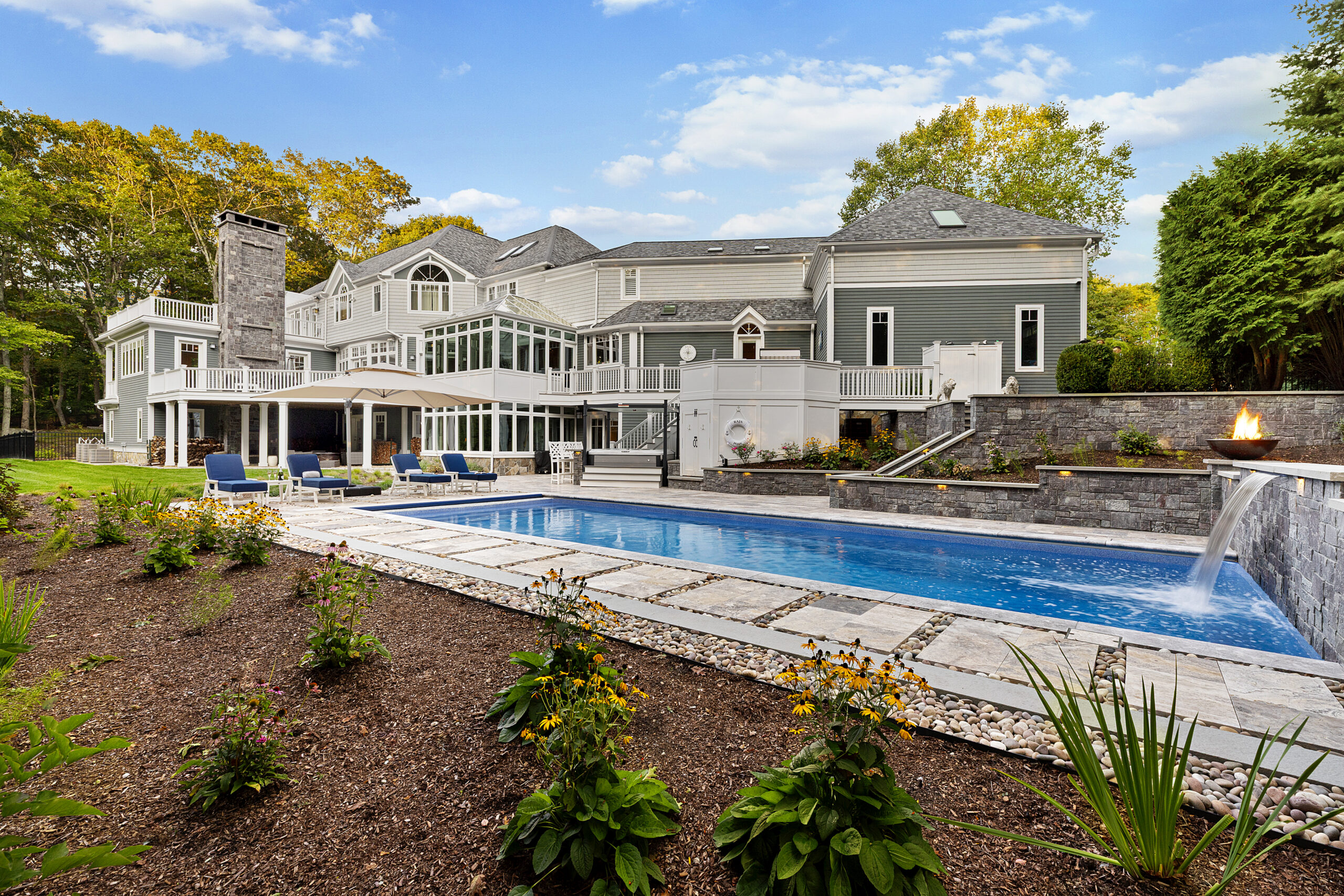 The pool area with the clients home in the background. Dex by Terra hardscape project in Lincoln, MA.