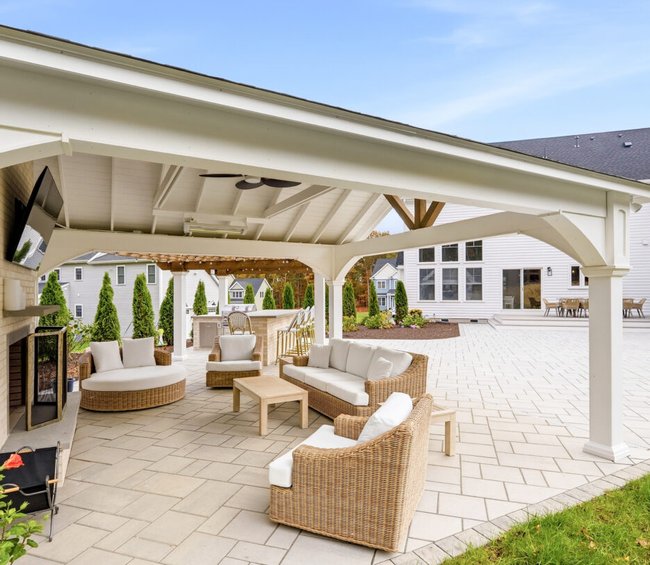 The patio pavilion seating area with home in the background. Outdoor living designed and built by Dex by Terra in North Attleboro, MA.