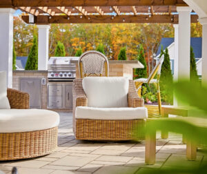 Seating under the patio pavilion with outdoor Kitchen in the background. Outdoor living designed and built by Dex by Terra in North Attleboro, MA.