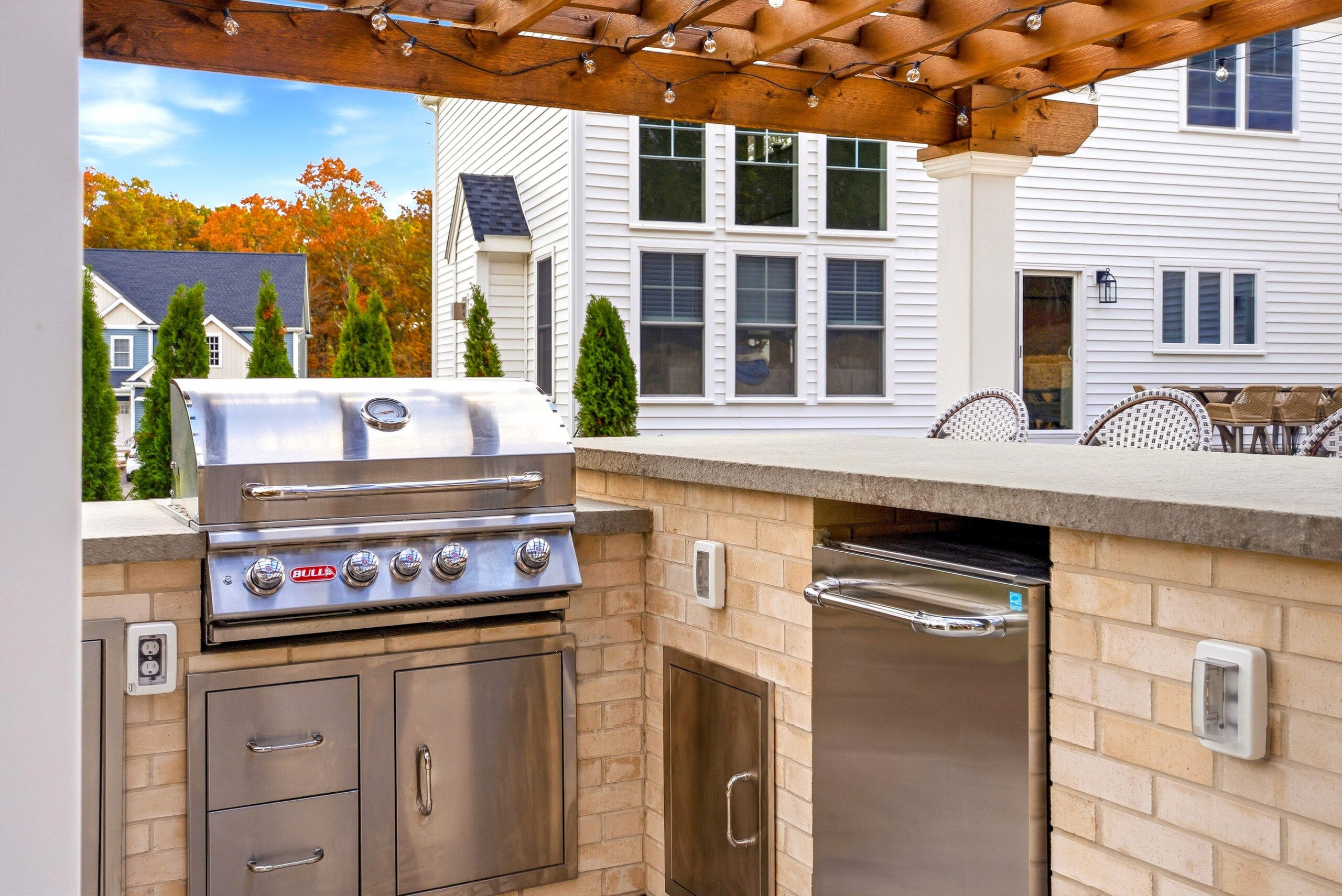 Outdoor kitchen with appliances by Bull Grills and Spas under a patio pergola, all designed and built by Dex by Terra in North Attleboro, MA.