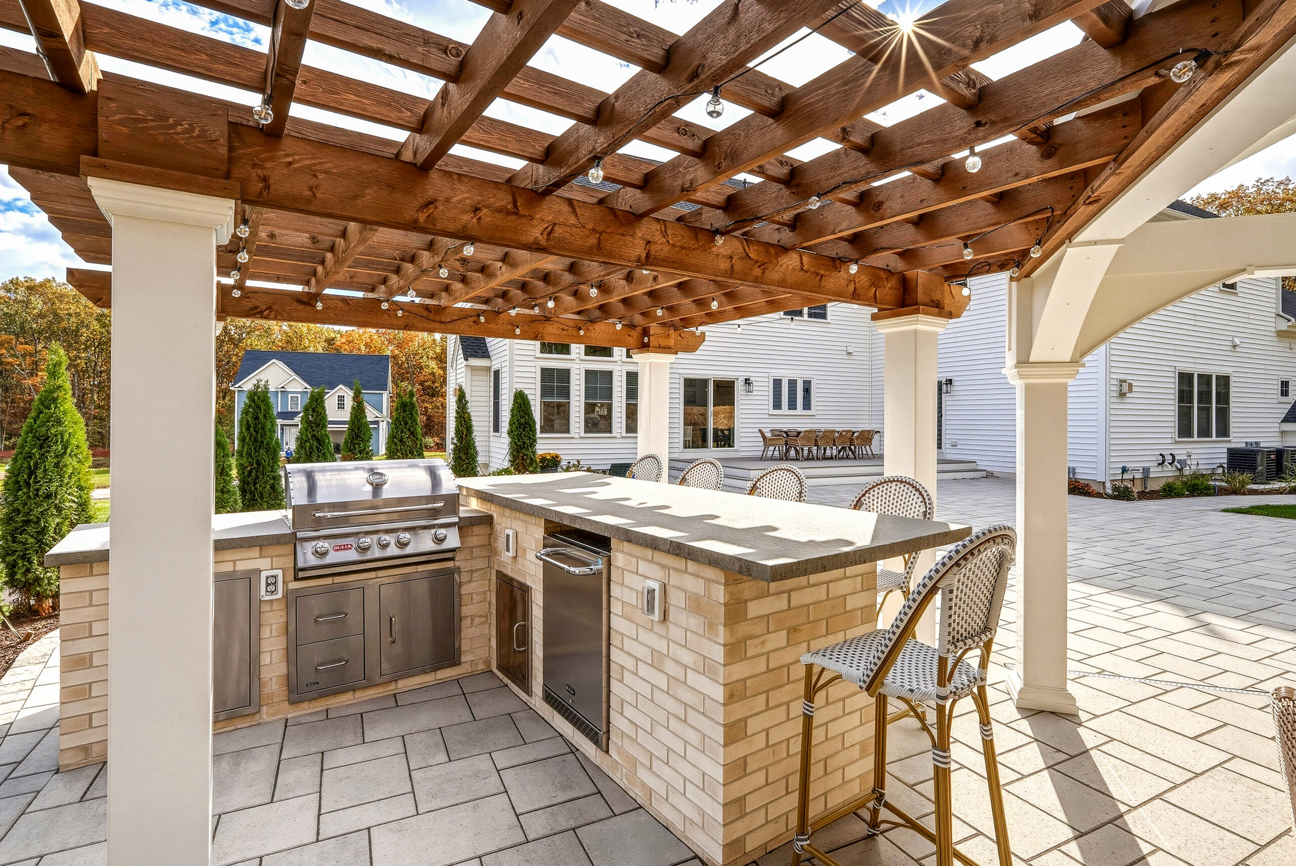 Outdoor kitchen with seating under a patio pergola, all designed and built by Dex by Terra in North Attleboro, MA.