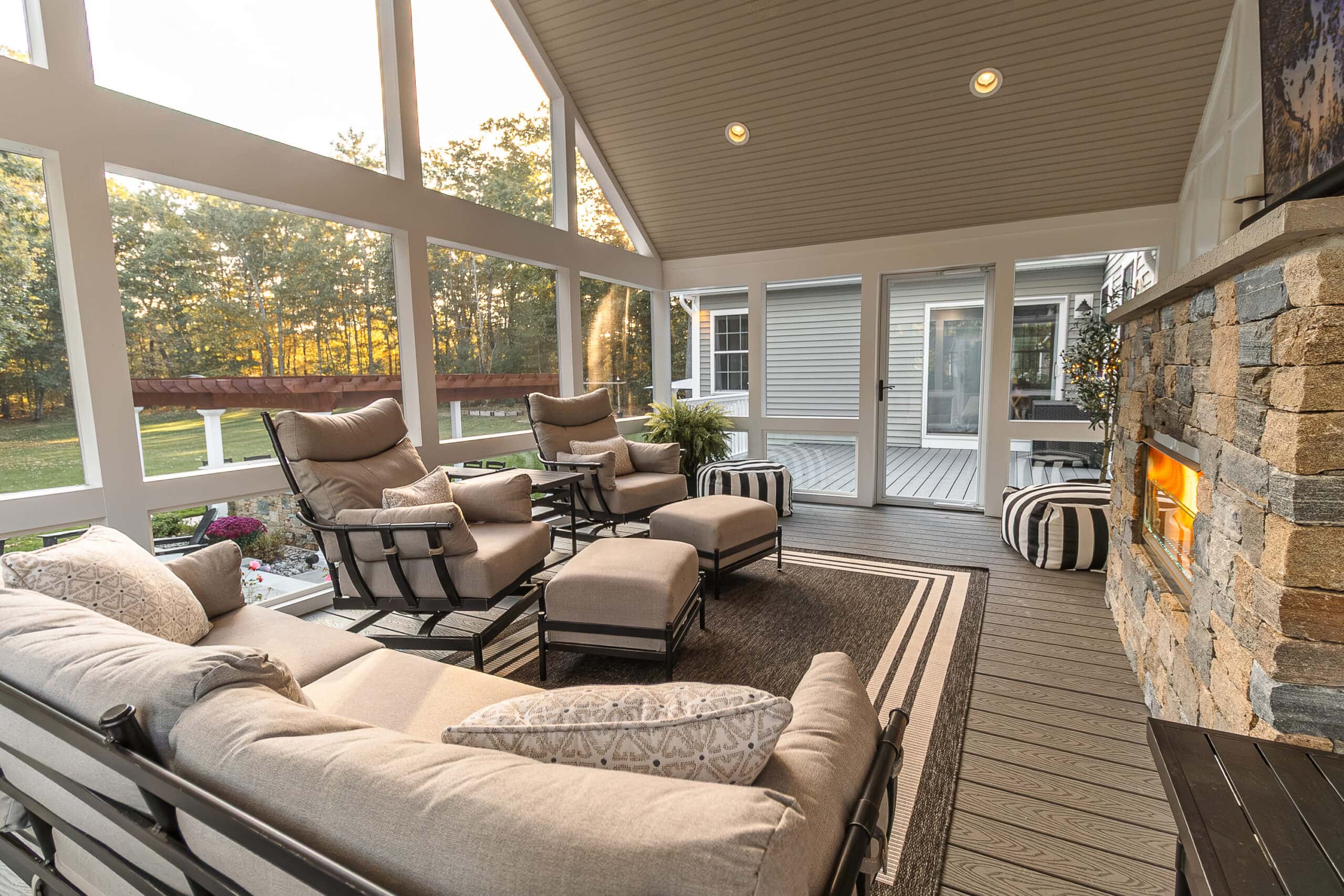 Interior of the three-season, screened-in porch with stone veneer gas fireplace insert. Trex decking. Landscape design in Dunstable, MA built by Dex by Terra.