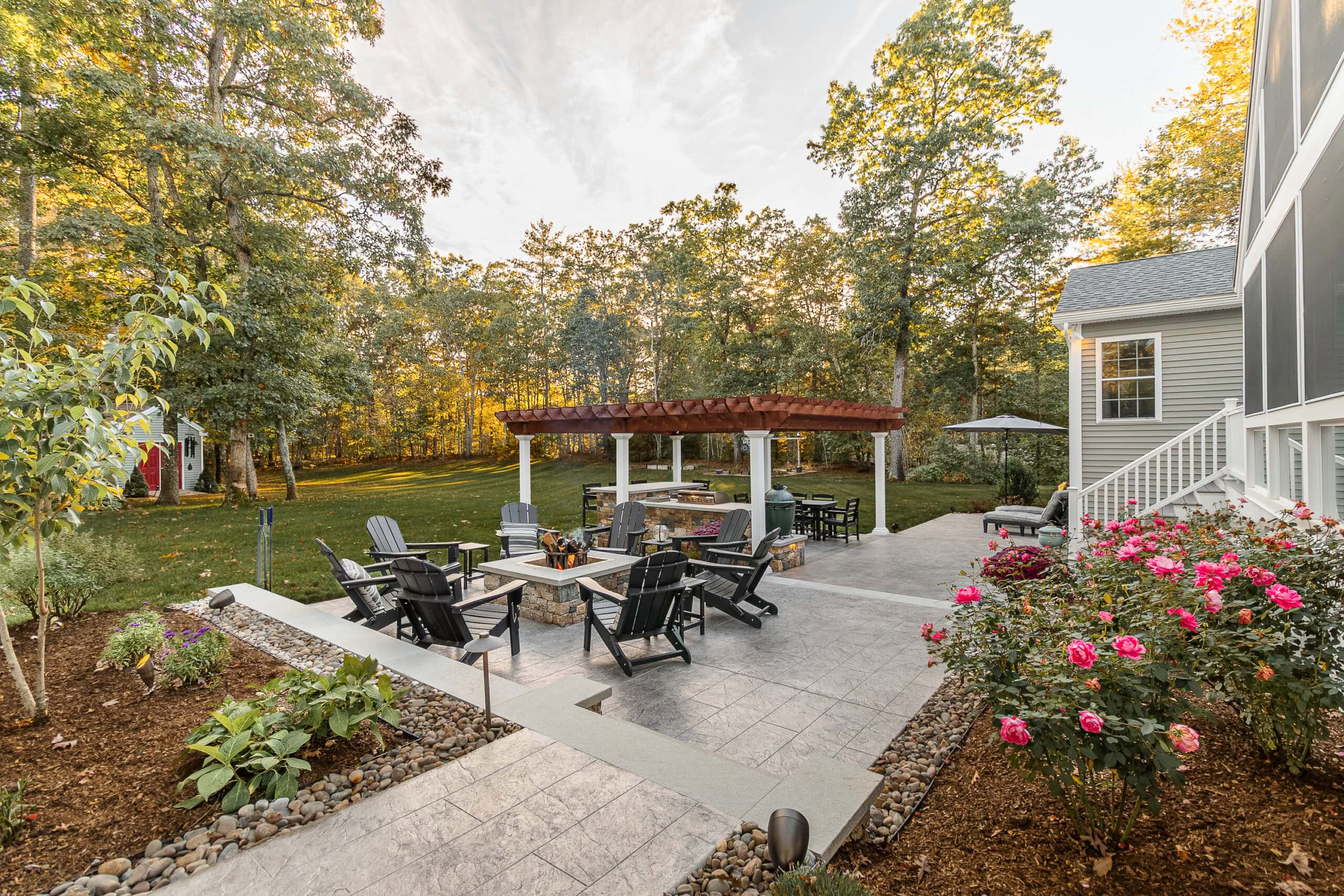 View of the fire pit patio, outdoor kitchen, pergola, and screened-in porch. Landscape design in Dunstable, MA built by Dex by Terra.