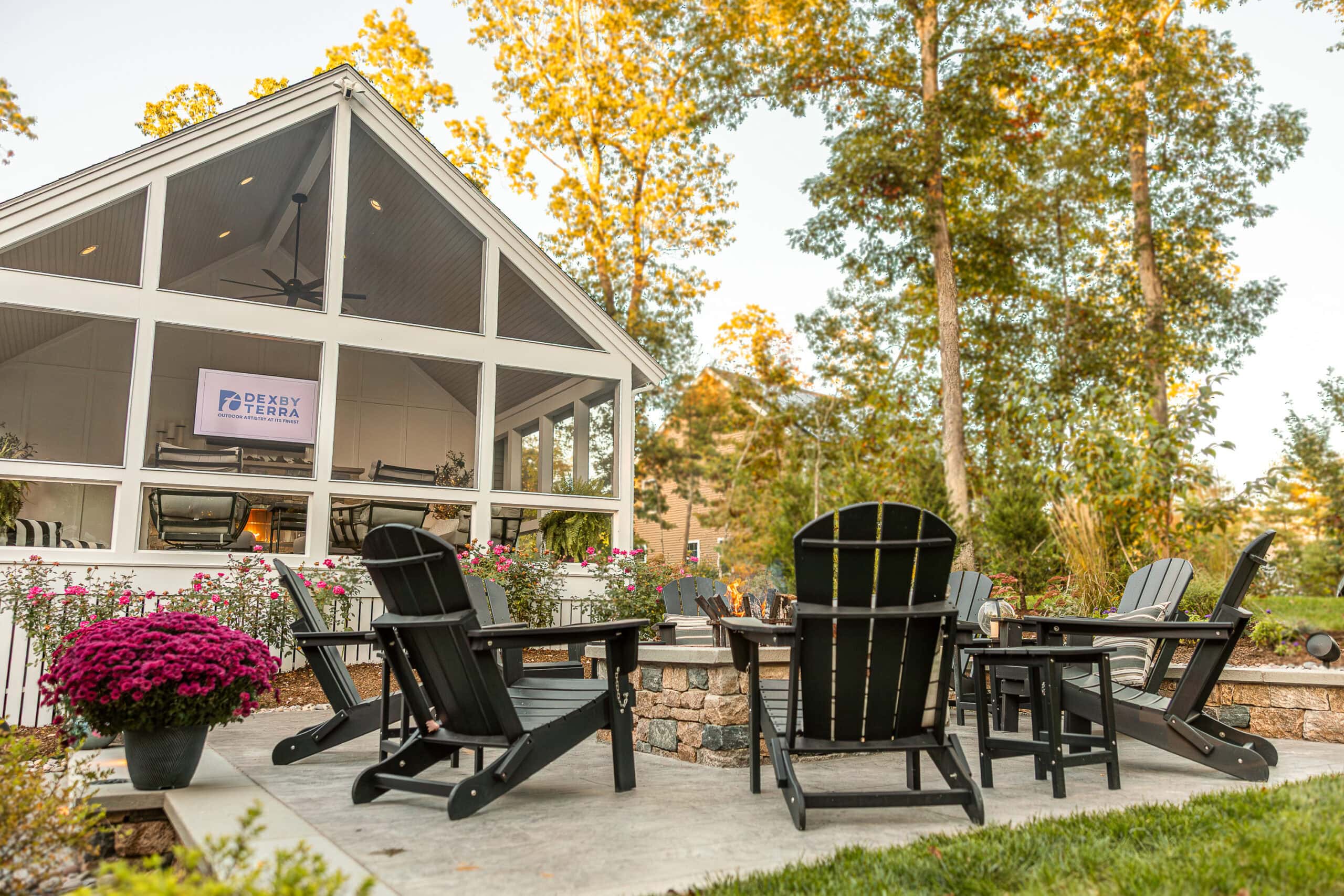 Wood burning fire pit with a three-season screened-in porch in the background. Landscape design in Dunstable, MA built by Dex by Terra.