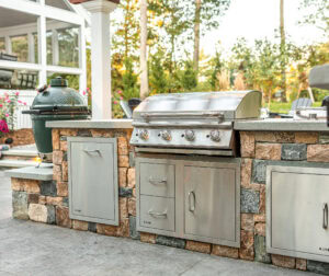 Stone veneer outdoor kitchen with stainless steel grill and storage cabinets in Dunstable, MA. Landscape design by Dex by Terra.