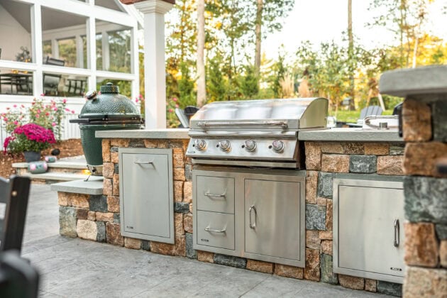 Stone veneer outdoor kitchen with stainless steel grill and storage cabinets in Dunstable, MA. Landscape design by Dex by Terra.