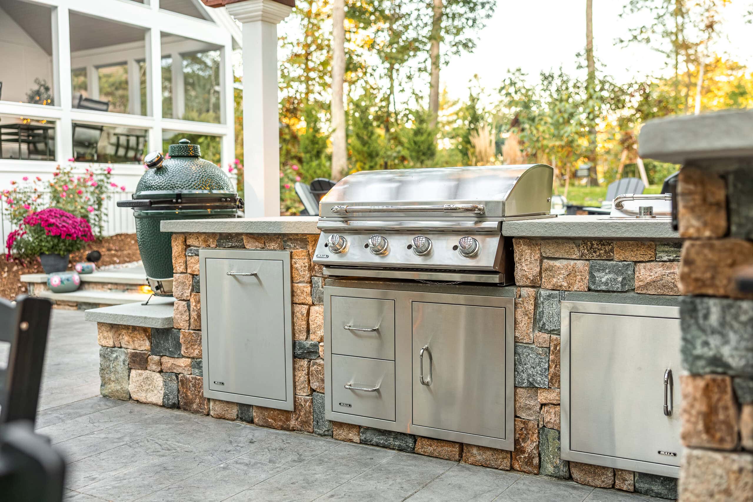 Stone veneer outdoor kitchen with stainless steel grill and storage cabinets in Dunstable, MA. Landscape design by Dex by Terra.