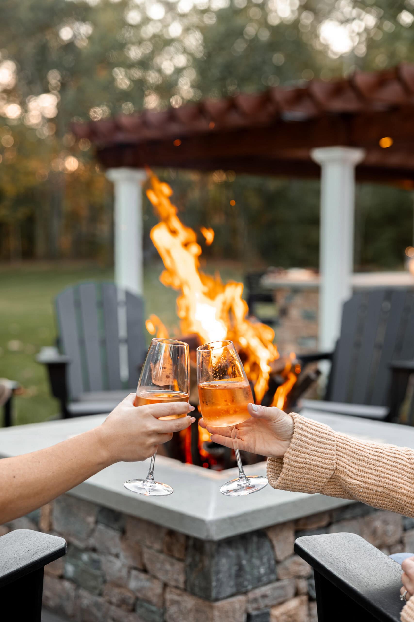 Two friends toast each other with drinks by the fire pit. Landscape design in Dunstable, MA built by Dex by Terra.