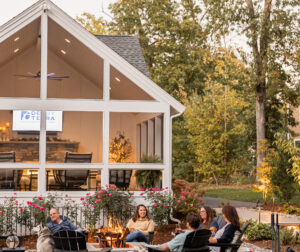 Friends enjoy the fire pit with the screened-in porch in the background as evening falls. Landscape design in Dunstable, MA built by Dex by Terra.