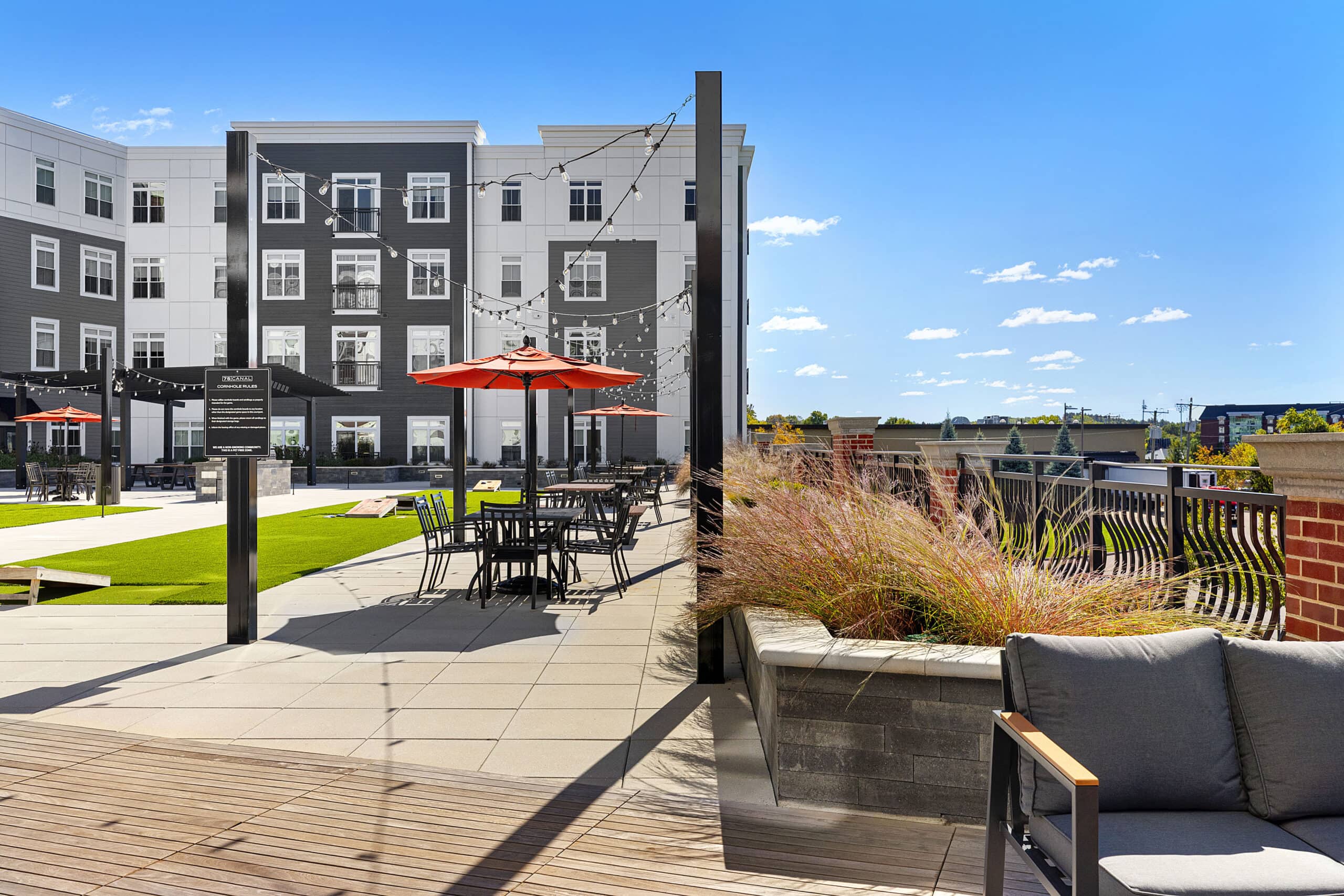 The second floor courtyard and amenity area with tables, chairs, and cornhole areas at 75 Canal Apartments in Manchester, NH.