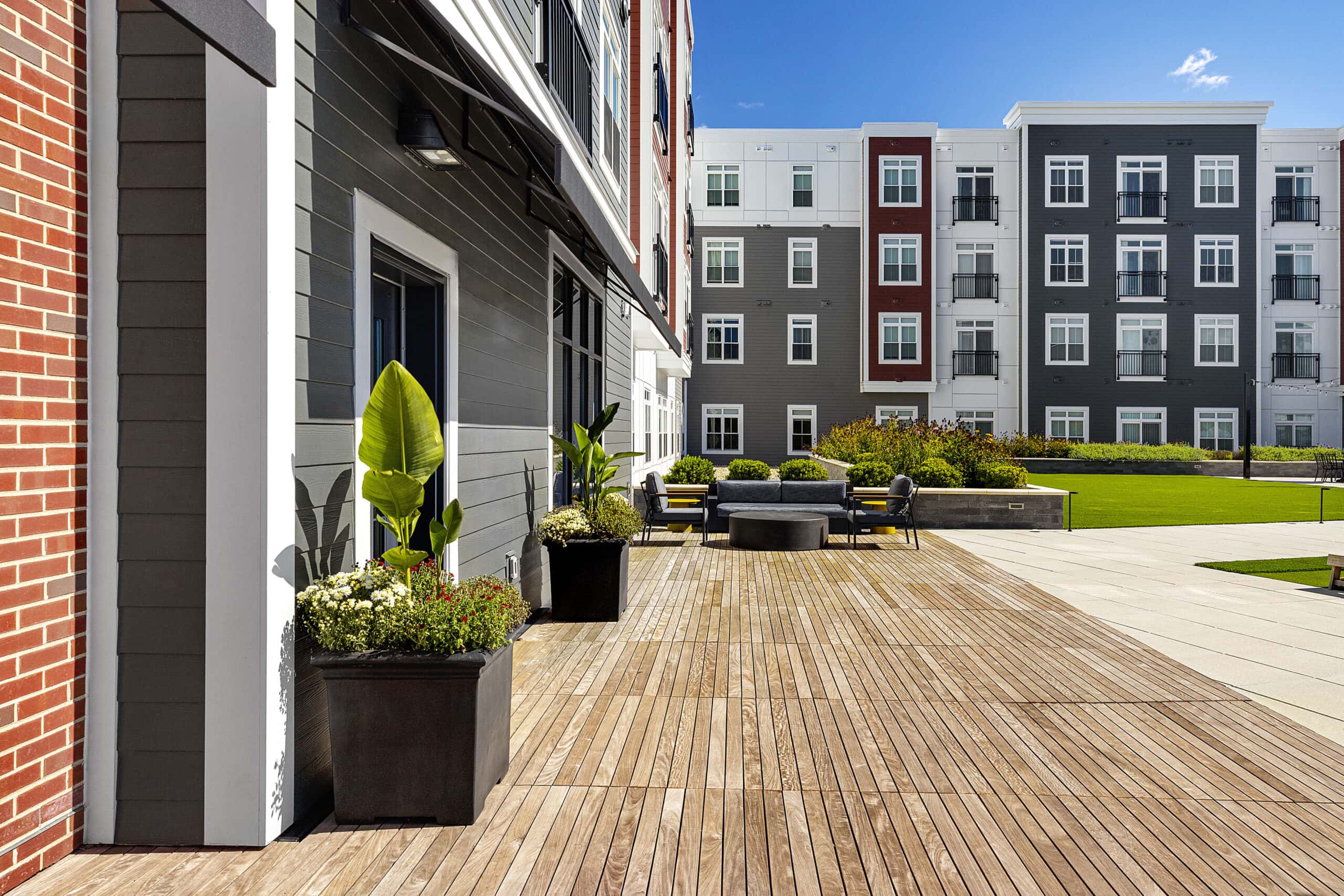 The second floor courtyard and amenity area with planters and seating area. Teak decking and concrete pavers with artificial turf in the background at 75 Canal Apartments in Manchester, NH. Hardscaping and landscaping by Dex by Terra of Hudson, MA.