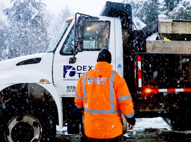 A Dex by Terra worker approaches a Dex By Terra Commercial Snow Removal & Management truck during a storm.