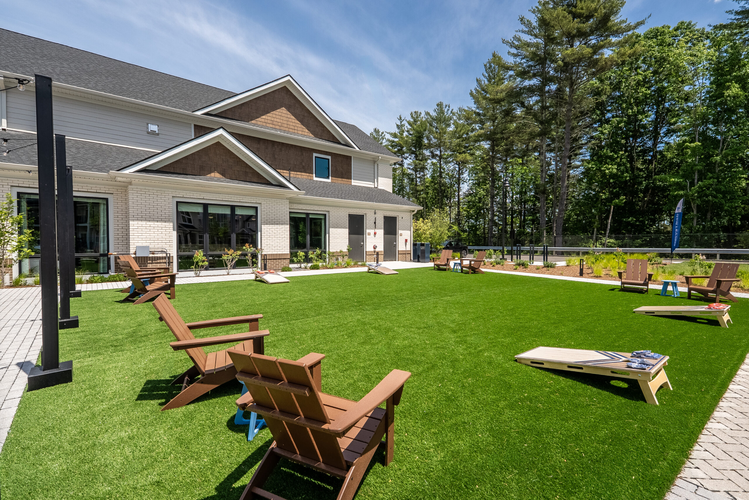 An artificial turf area for corn hole and other activities, with the clubhouse in the background at The Penstone Apartments in Walpole, MA. Hardscaping and landscaping by Dex by Terra of Hudson, MA.