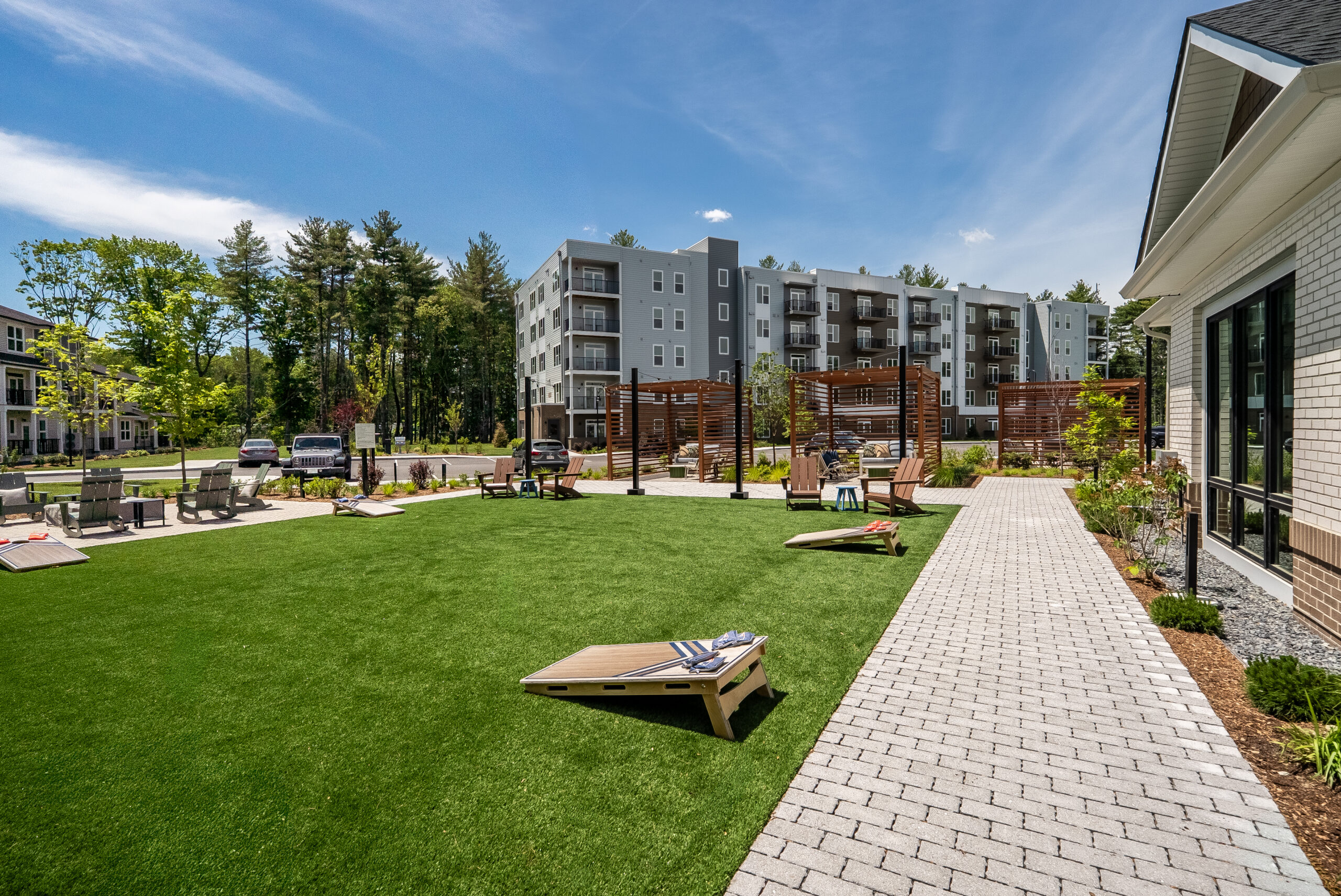 An artificial turf area for corn hole and other activities, with a paver walkway at The Penstone Apartments in Walpole, MA. Hardscaping and landscaping by Dex by Terra of Hudson, MA.