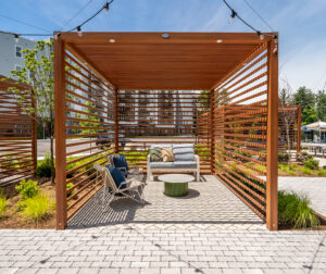 A pergola provides shade for a seating area at The Penstone Apartments in Walpole, MA. Hardscaping and landscaping by Dex by Terra of Hudson, MA.