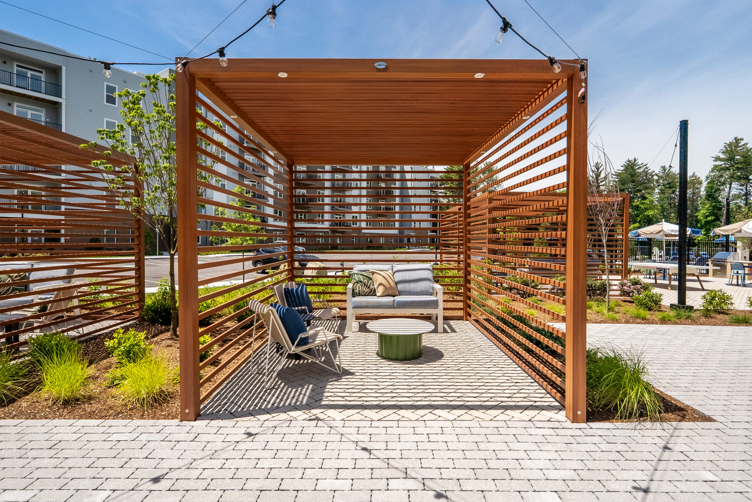 A pergola provides shade for a seating area at The Penstone Apartments in Walpole, MA. Hardscaping and landscaping by Dex by Terra of Hudson, MA.