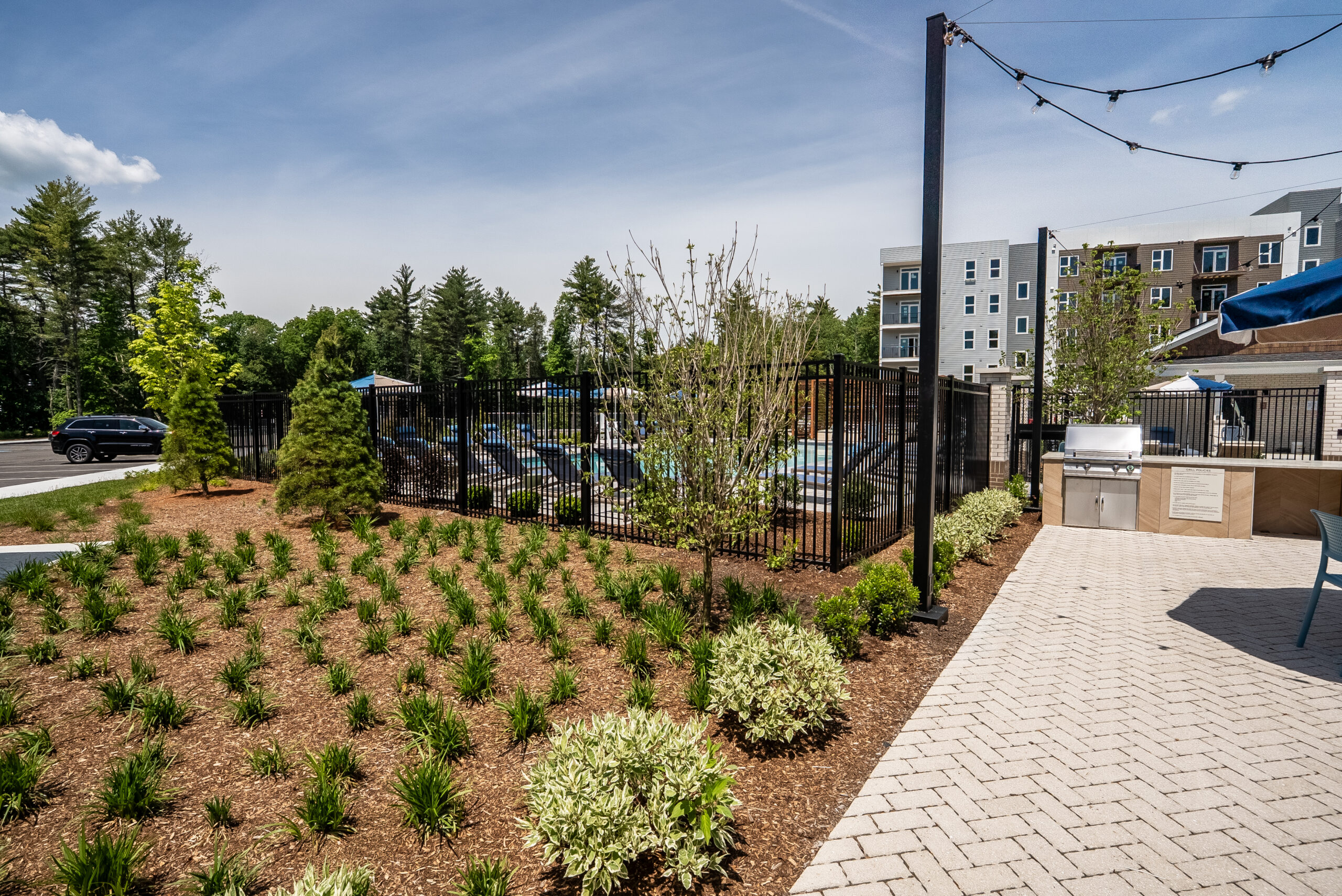 Mulched plant beds soften the border of the grill station amenity area at The Penstone Apartments in Walpole, MA. Hardscaping and landscaping by Dex by Terra of Hudson, MA.