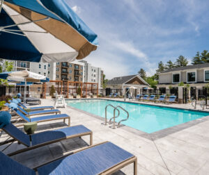 The pool area with seating shaded by umbrellas at The Penstone Apartments in Walpole, MA. Hardscaping and landscaping by Dex by Terra of Hudson, MA.