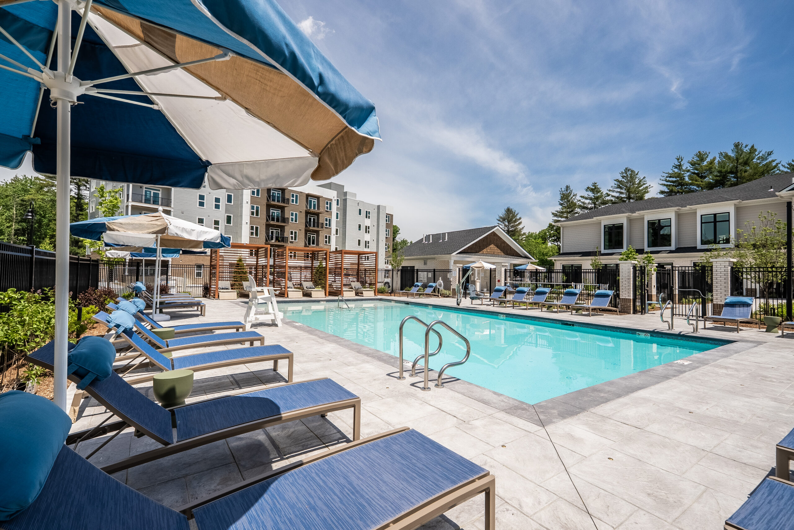 The pool area with seating shaded by umbrellas at The Penstone Apartments in Walpole, MA. Hardscaping and landscaping by Dex by Terra of Hudson, MA.