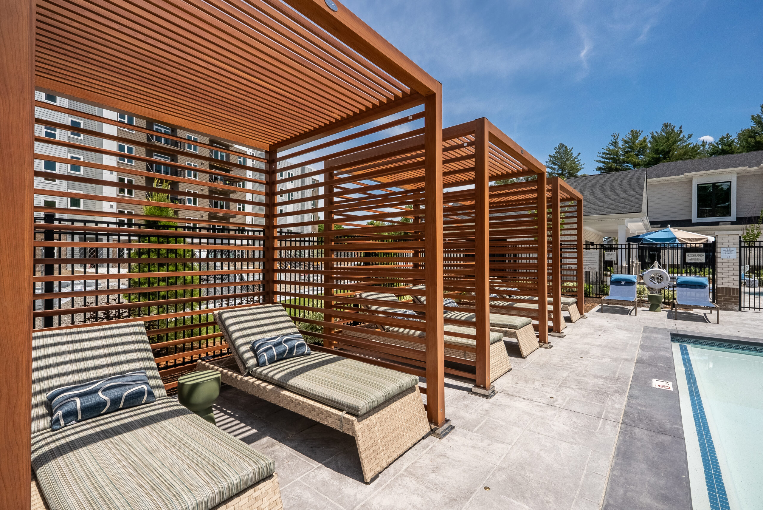 Modern pergolas provide shade and privacy for poolside lounge chairs at The Penstone Apartments in Walpole, MA. Hardscaping and landscaping by Dex by Terra of Hudson, MA.